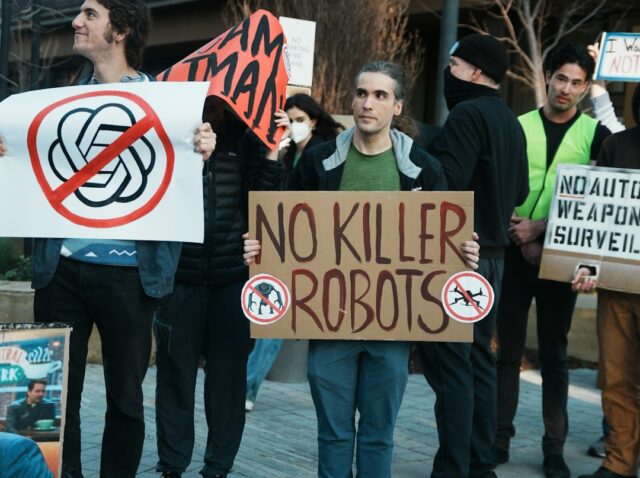 Protesters hold signs against killer robots and ai.