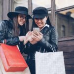 Two women looking at a smartphone with shopping bags