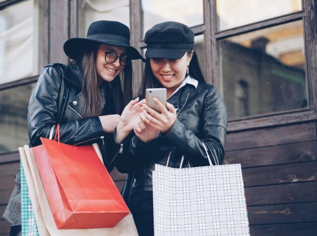 Two women looking at a smartphone with shopping bags